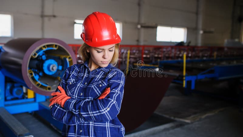 Beautiful woman in red safety helmet work as industrial worker at metal sheet profiling mechine at manufacturing factory