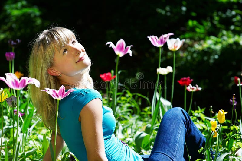 Beautiful woman sitting on the grass among flowers