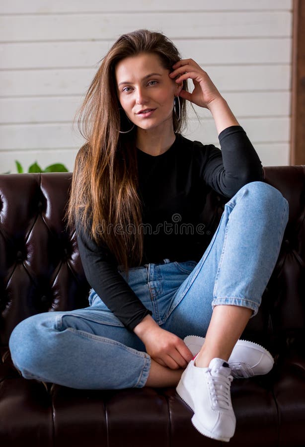 Beautiful Woman Sitting on a Sofa in Jeans and Sneakers at Home Stock ...