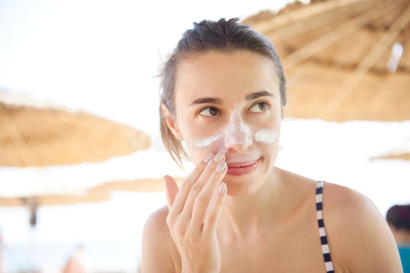 Beautiful woman smears face sunscreen at the beach for protection