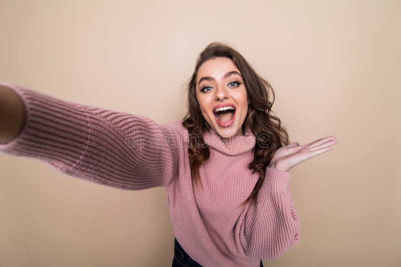 Beautiful woman smiling with white teeth and making selfie, photographing herself over brown background