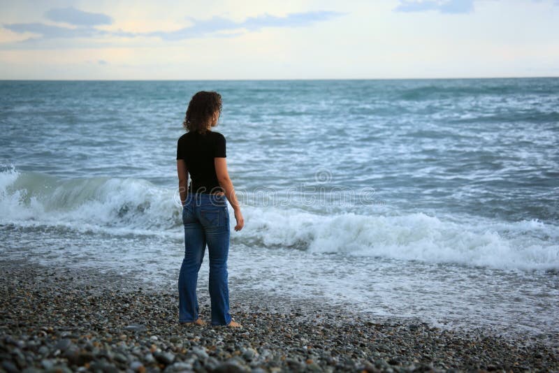 Beautiful woman on stone seacoast, Standing back