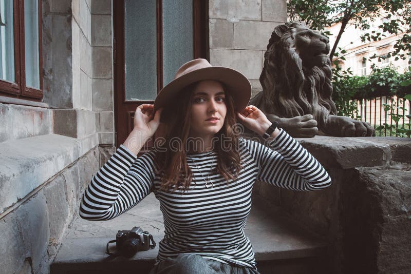 Beautiful woman in a striped shirt and hat. Holds the camera near the statue of a lion against the background of the old royalty free stock photography Beautiful woman in a striped shirt and hat. Holds the camera near the statue of a lion against the background of the old royalty free stock photography