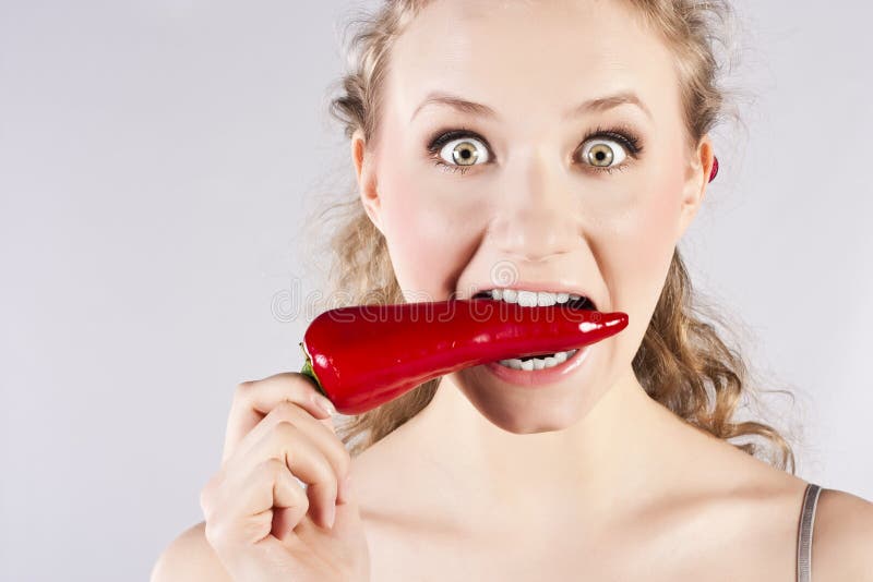 Beautiful woman teeth eating red hot chili pepper