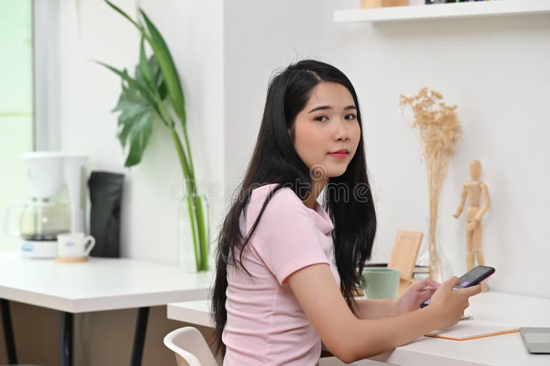 A beautiful woman is using a smartphone while sitting at the white working desk royalty free stock images