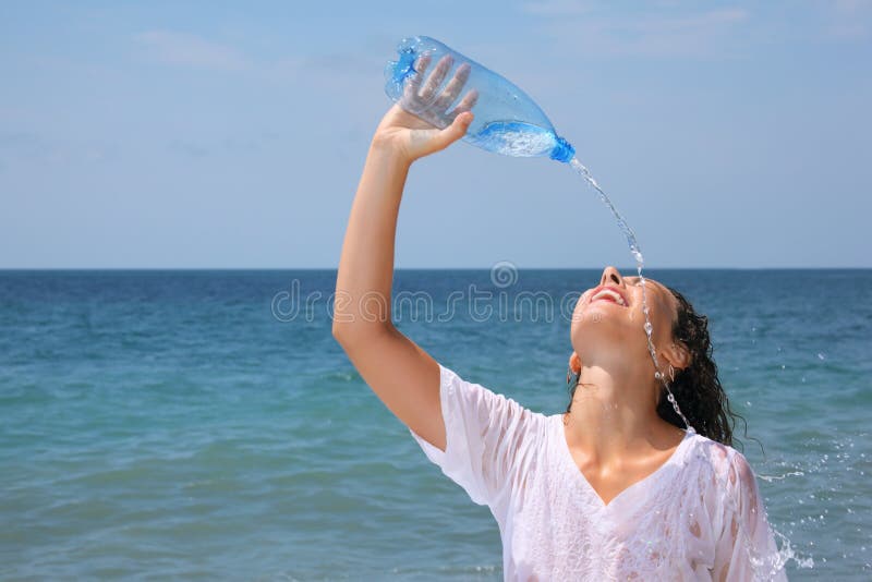 Beautiful woman watering from bottle on seacoast stock photo
