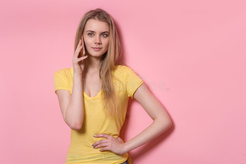 Beautiful young adult woman talking on mobile phone standing near pink wall