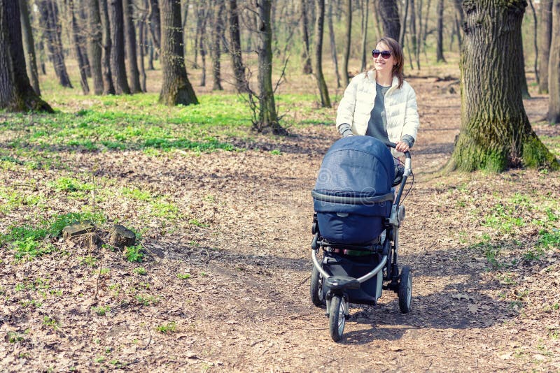 Beautiful young adult woman walking with baby in stroller through forest or park on bright sunny day. Healthy lifestyle and royalty free stock images Beautiful young adult woman walking with baby in stroller through forest or park on bright sunny day. Healthy lifestyle and royalty free stock images