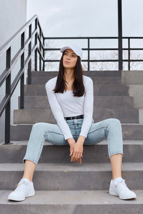 Beautiful Young Adult Woman Wearing Jeans, White Shirt and Baseball Cap  Sitting on Stairs Outdoors and Looking Away, Having Stock Photo - Image of  model, outside: 216612278