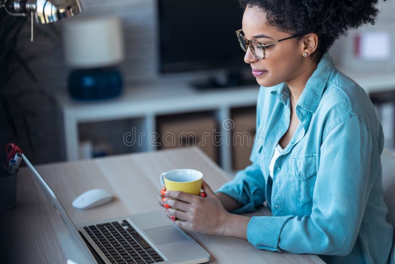 Beautiful young afro business woman making video call with laptop while drinking coffee sitting in the office at home