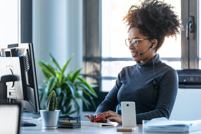 Beautiful young afro business woman working while making video call with computer sitting in the office