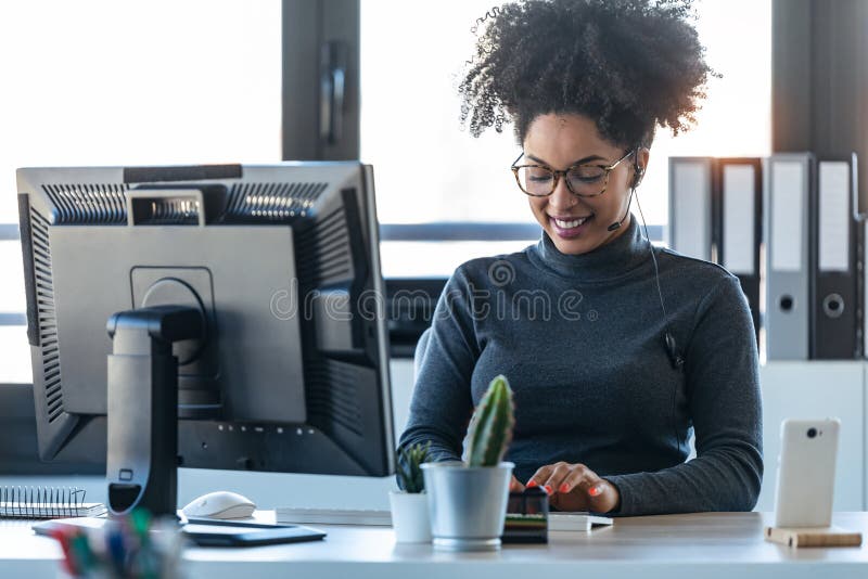 Beautiful young afro business woman working while making video call with computer sitting in the office