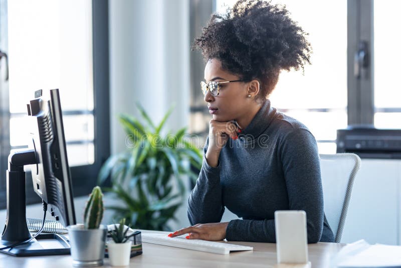 Beautiful young afro business woman working while making video call with computer sitting in the office