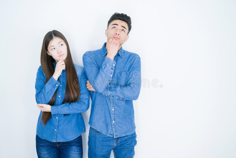 Beautiful young asian couple over white isolated background with hand on chin thinking about question, pensive expression royalty free stock photo