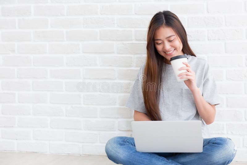 Beautiful young of Asian girl using a laptop while sitting at the floor in the living room and hold coffee, Asia women smile while. Beautiful young of Asian girl royalty free stock images Beautiful young of Asian girl using a laptop while sitting at the floor in the living room and hold coffee, Asia women smile while. Beautiful young of Asian girl royalty free stock images
