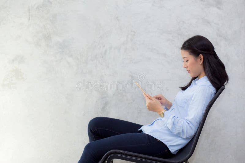 Beautiful young asian woman touching tablet computer and smile sitting on cement background