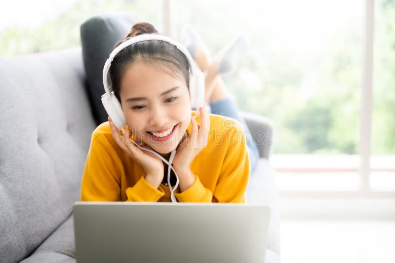 Beautiful young asian woman using laptop and wearing headphones listening to music