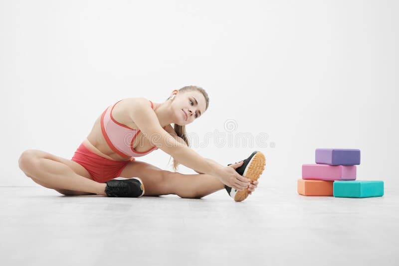 Beautiful young athletic woman in sneakers and red sportswear doing stretching on the floor. Multi-colored blocks for stock images Beautiful young athletic woman in sneakers and red sportswear doing stretching on the floor. Multi-colored blocks for stock images