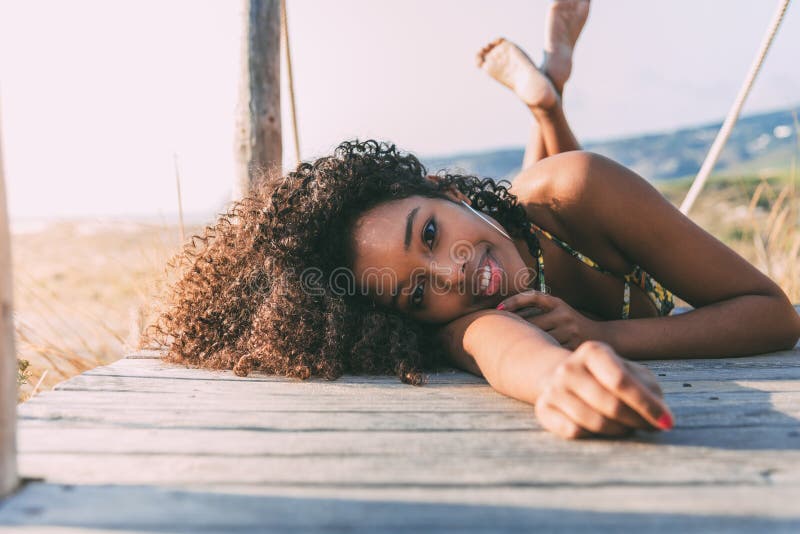 Beautiful young black woman lying down in a wooden foot bridge