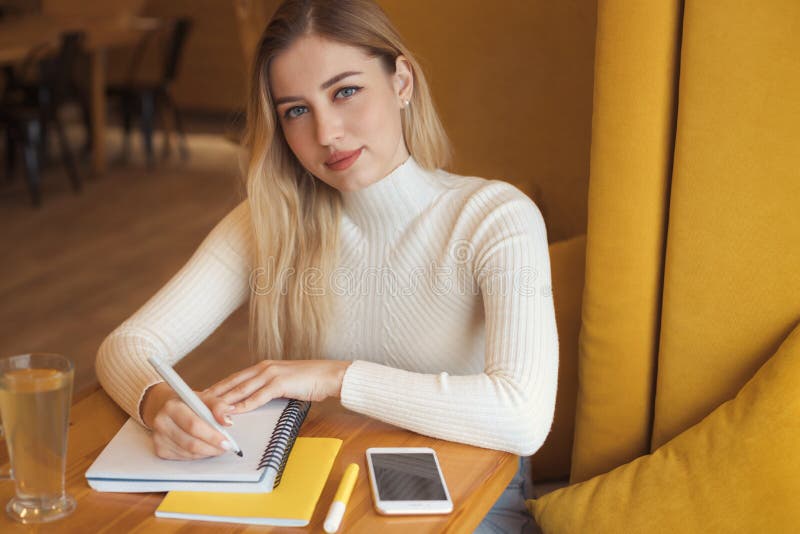 Portrait of a beautiful young blonde student girl with long hair sitting in cafe and studying