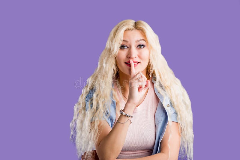 A beautiful young blonde woman with her finger to her lips saying shh. Copy space on purple background royalty free stock photos A beautiful young blonde woman with her finger to her lips saying shh. Copy space on purple background royalty free stock photos
