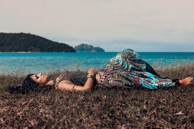 Beautiful young boho woman lying on a grass at the beach