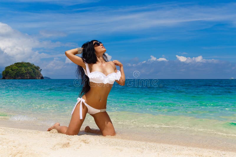 Beautiful young brunette in white bikini on a tropical beach. S