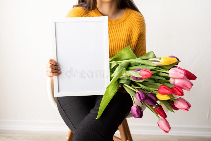 Beautiful young brunette woman with bouquet of fresh pink tulips and blank frame for mock up