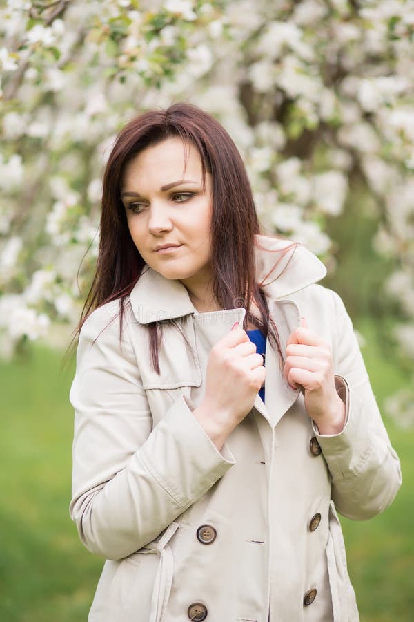 Beautiful Young Brunette Woman Standing Near The Blossoming Apple Tree On A Warm Spring Day