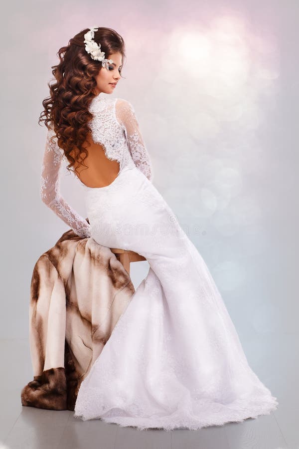 Beautiful young brunette woman in a wedding dress sits on a mink coat back royalty free stock photography Beautiful young brunette woman in a wedding dress sits on a mink coat back royalty free stock photography