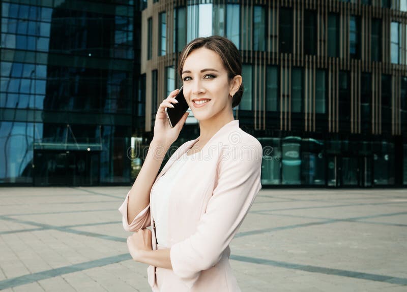 Beautiful young business woman uses a mobile phone in front of a modern business center