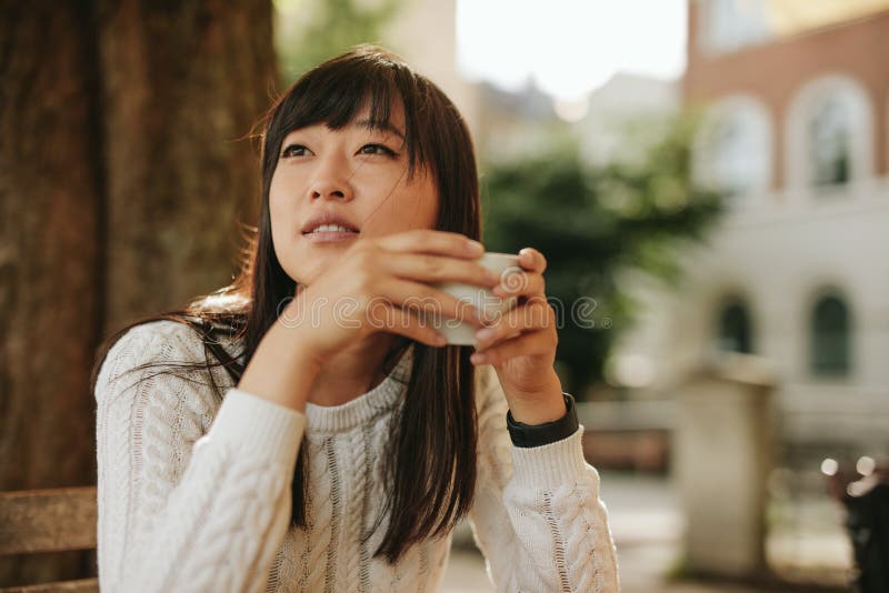 Shot of beautiful young chinese woman with cup of coffee sitting at outdoor cafe and looking away. Shot of beautiful young chinese woman with cup of coffee sitting at outdoor cafe and looking away.