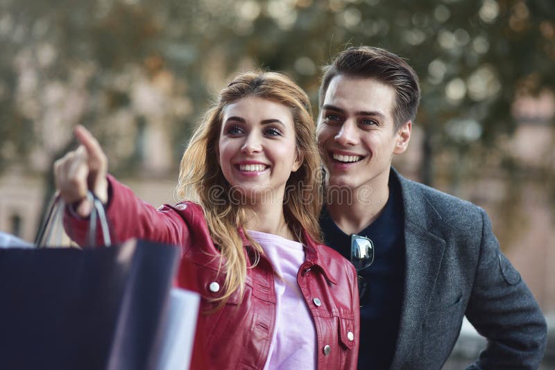 Beautiful couple with shopping bags is talking and smiling while doing shopping in the mall focus on the woman. Beautiful couple with shopping bags is talking and smiling while doing shopping in the mall focus on the woman