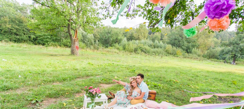 Beautiful Young Couple Having Picnic in Countryside. Happy Family Outdoor. Smiling Man and Woman relaxing in Park. Relationships