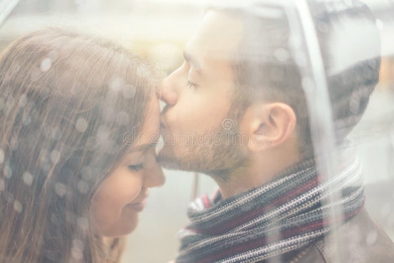 Beautiful young couple having a romantic tender moment under the rain - Handsome man kissing his girlfriend forehead