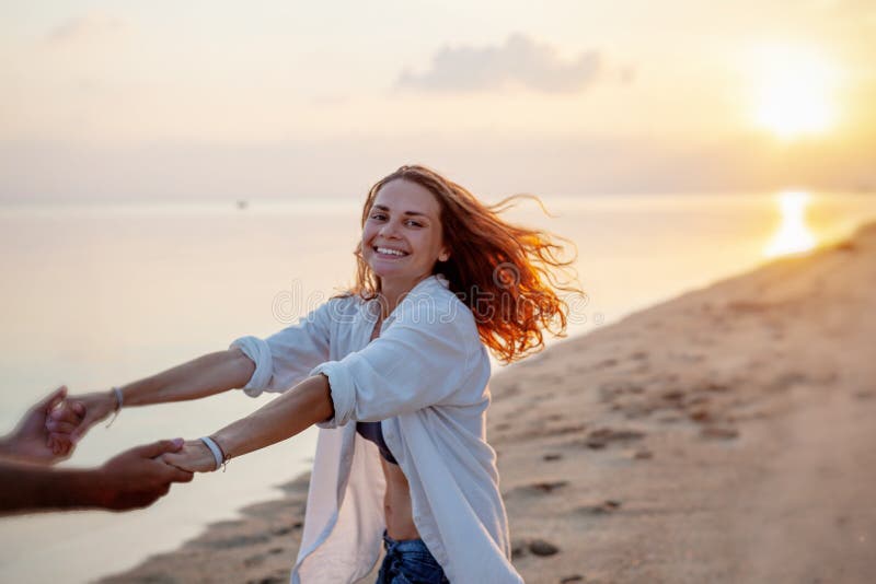 Beautiful young couple in love whirls holding hands on the beach at sunset during the honeymoon vacation travel royalty free stock photo Beautiful young couple in love whirls holding hands on the beach at sunset during the honeymoon vacation travel royalty free stock photo