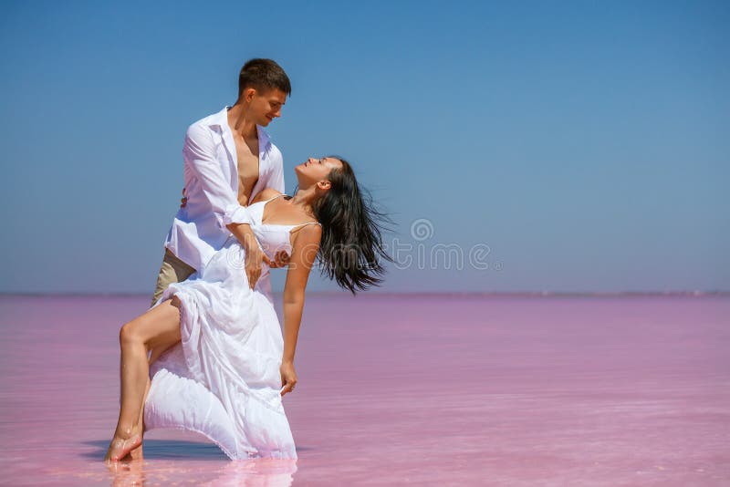 Beautiful young couple in white clothes dancing on a pink lake in the afternoon the sun is shining