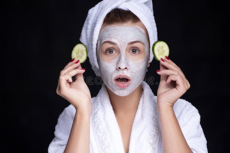 Beautiful young european woman apply clay mask on her face with towel on her head and cucumbers on her eyes. beauty spa concept stock images Beautiful young european woman apply clay mask on her face with towel on her head and cucumbers on her eyes. beauty spa concept stock images