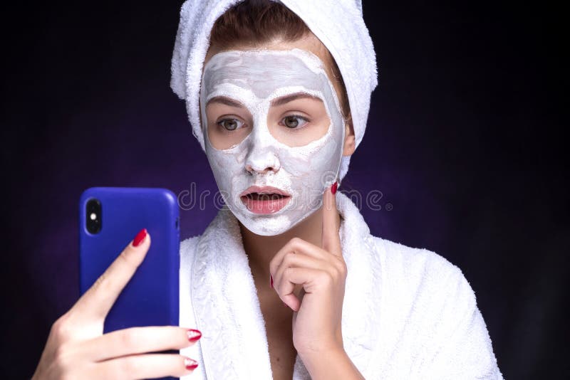 Beautiful young european woman apply clay mask on her face with towel on her head. She make selfie. Beauty spa concept stock image Beautiful young european woman apply clay mask on her face with towel on her head. She make selfie. Beauty spa concept stock image