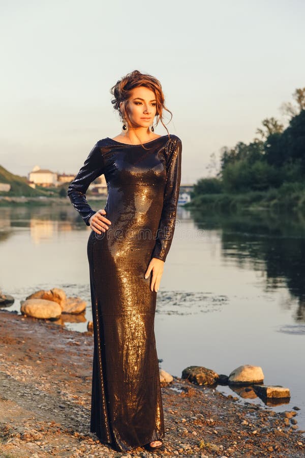 Beautiful young fashionable woman posing in dress at the river coast