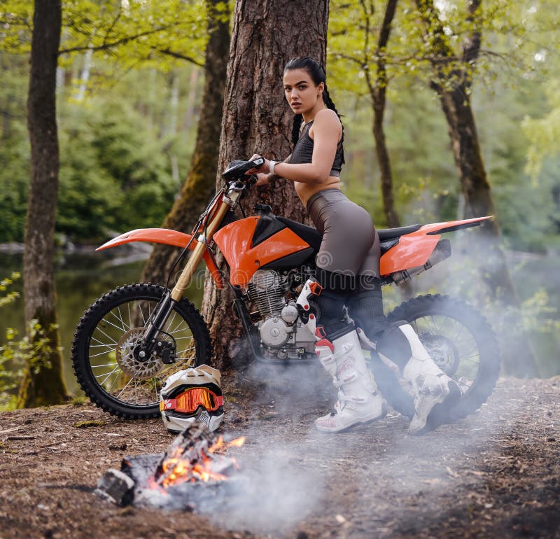 Charming Young Female Racer Wearing Motocross Outfit with Semi Naked Torso Leans Her Motorcycle