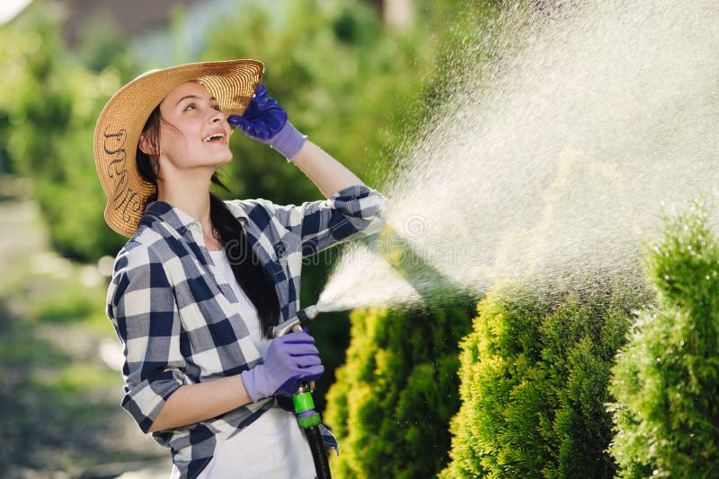 Beautiful young gardener woman watering garden in hot summer day