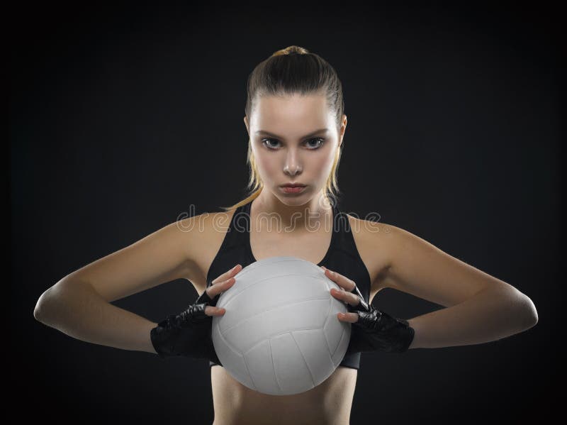 Beautiful young girl athlete in a black top with an aggressive pose and facial expressions with a ball for volleyball on a black background.