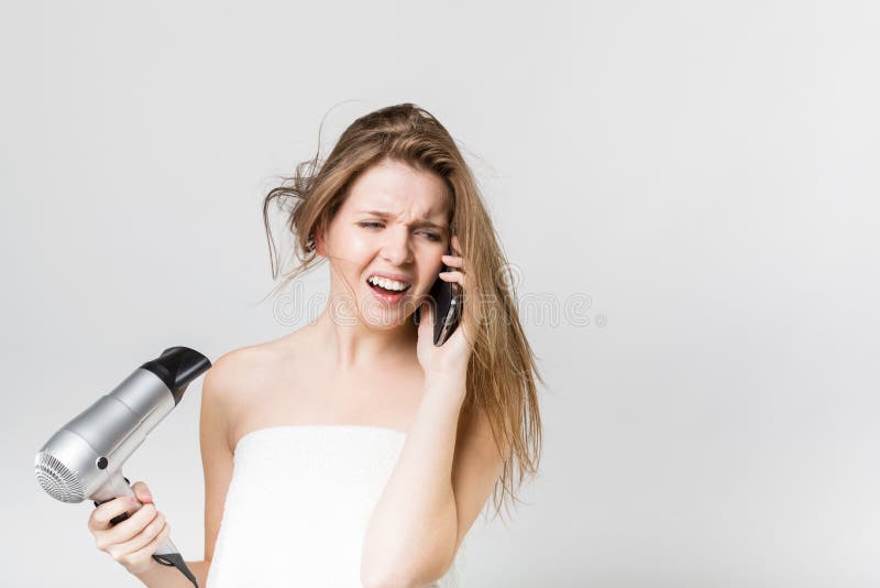 Beautiful young girl blow drying her hair while talking on the s