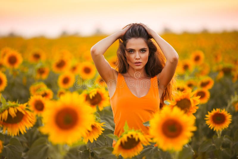 Beautiful young girl enjoying nature on the field of sunflowers at sunset. Summertime. Attractive brunette woman with long healthy