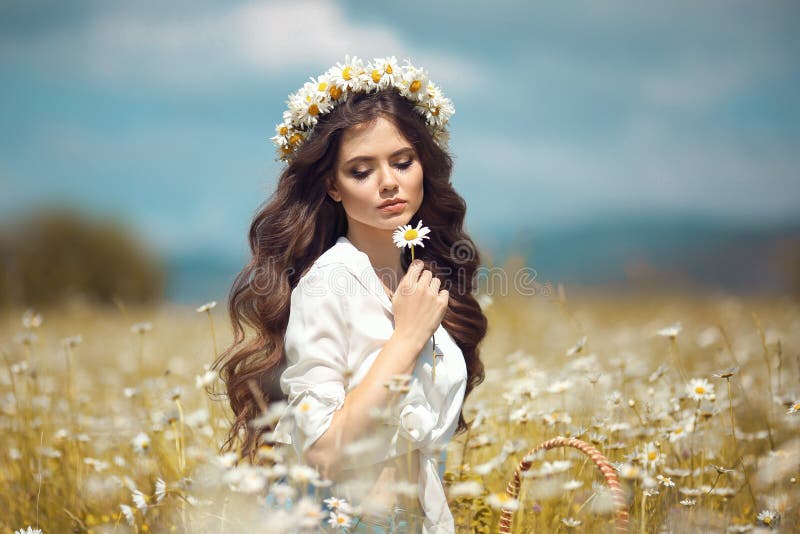 Beautiful young girl with flower enjoying in chamomile field. Carefree happy brunette woman with chaplet on healthy wavy hair