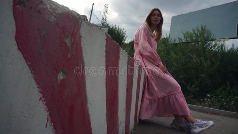 Girl in pink dress sits on concrete block, an empty billboard on the background