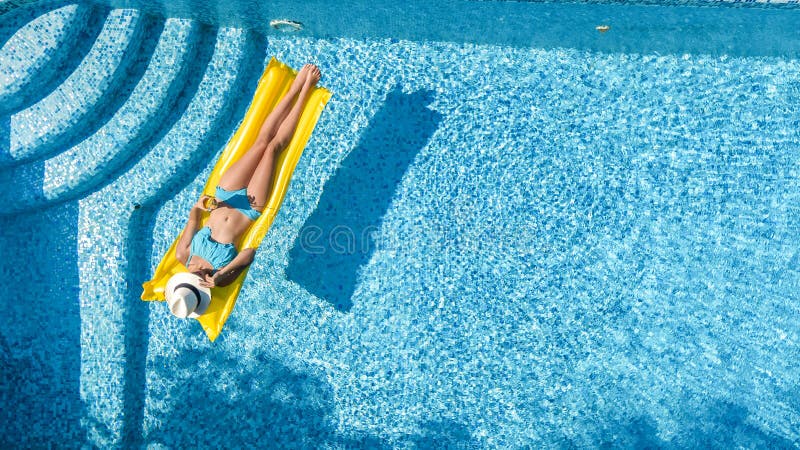 Beautiful young girl relaxing in swimming pool, swims on inflatable mattress and has fun in water on family vacation, aerial view