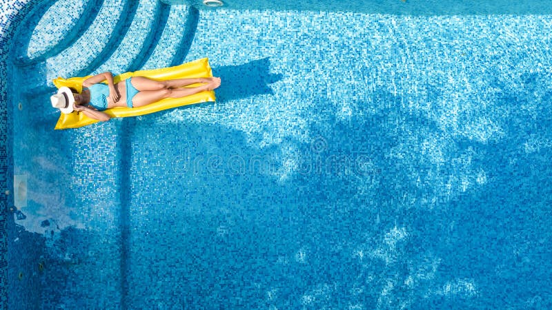 Beautiful young girl relaxing in swimming pool, swims on inflatable mattress and has fun in water on family vacation