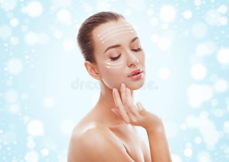Beautiful young girl touching her face on blue background and snow. Plastic surgery, facelift and rejuvenation concept.